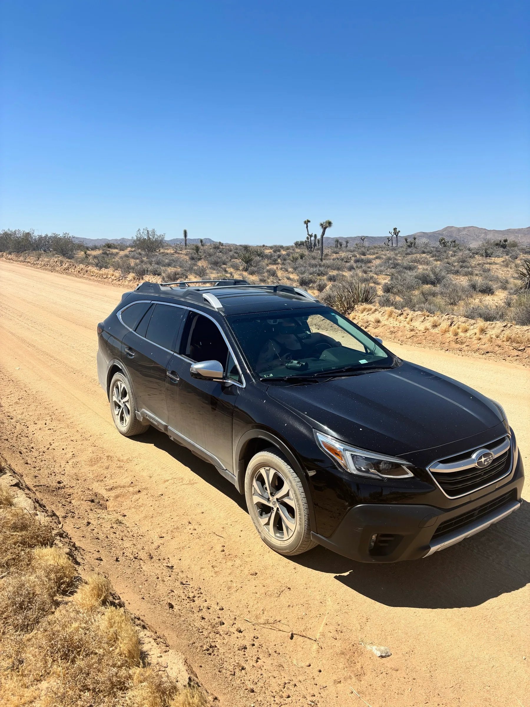 A black Subaru Outback parked on a sandy desert road