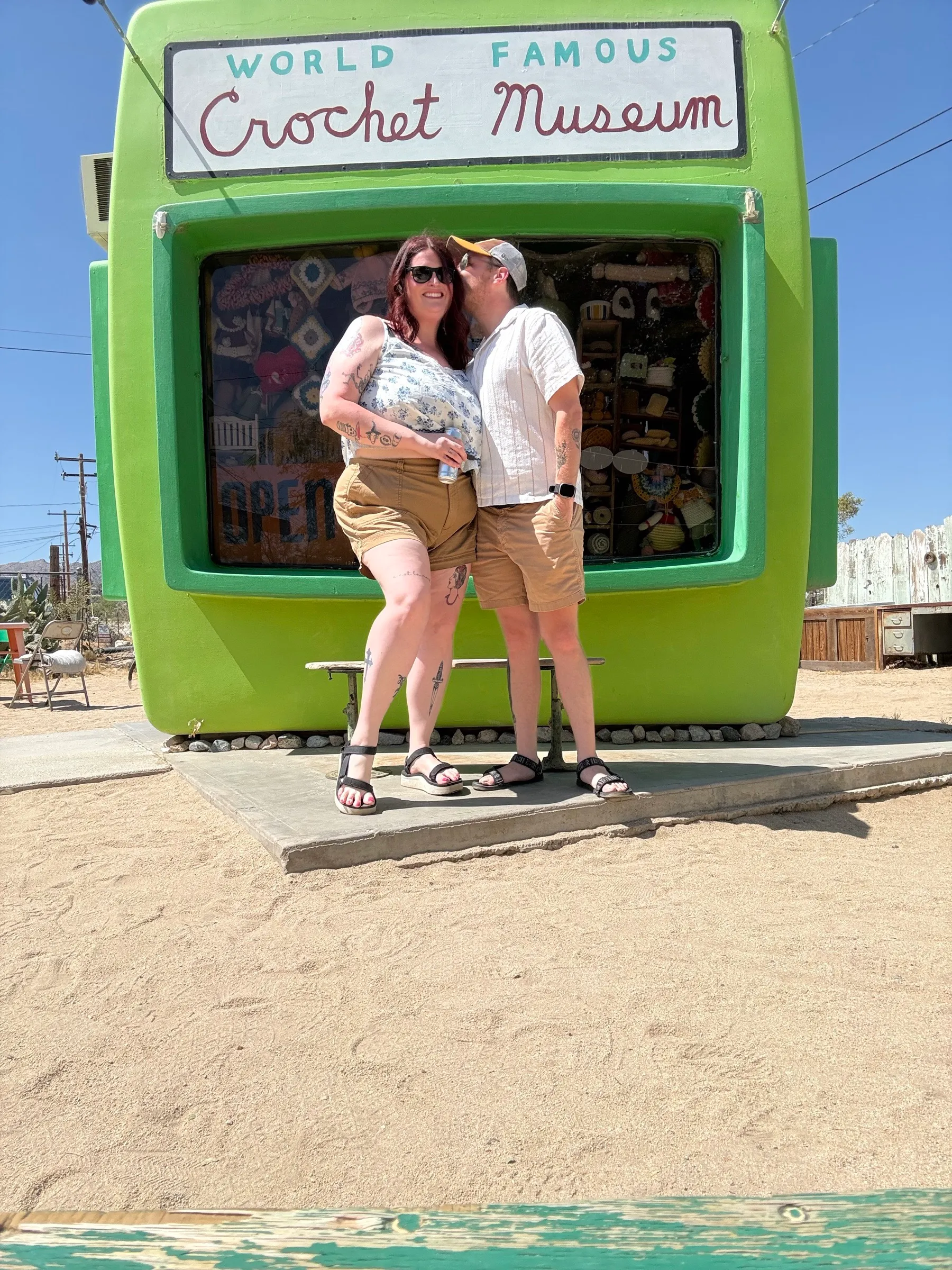 Two people in front of the World Famous Crochet Museum, a lime-green former photo kiosk