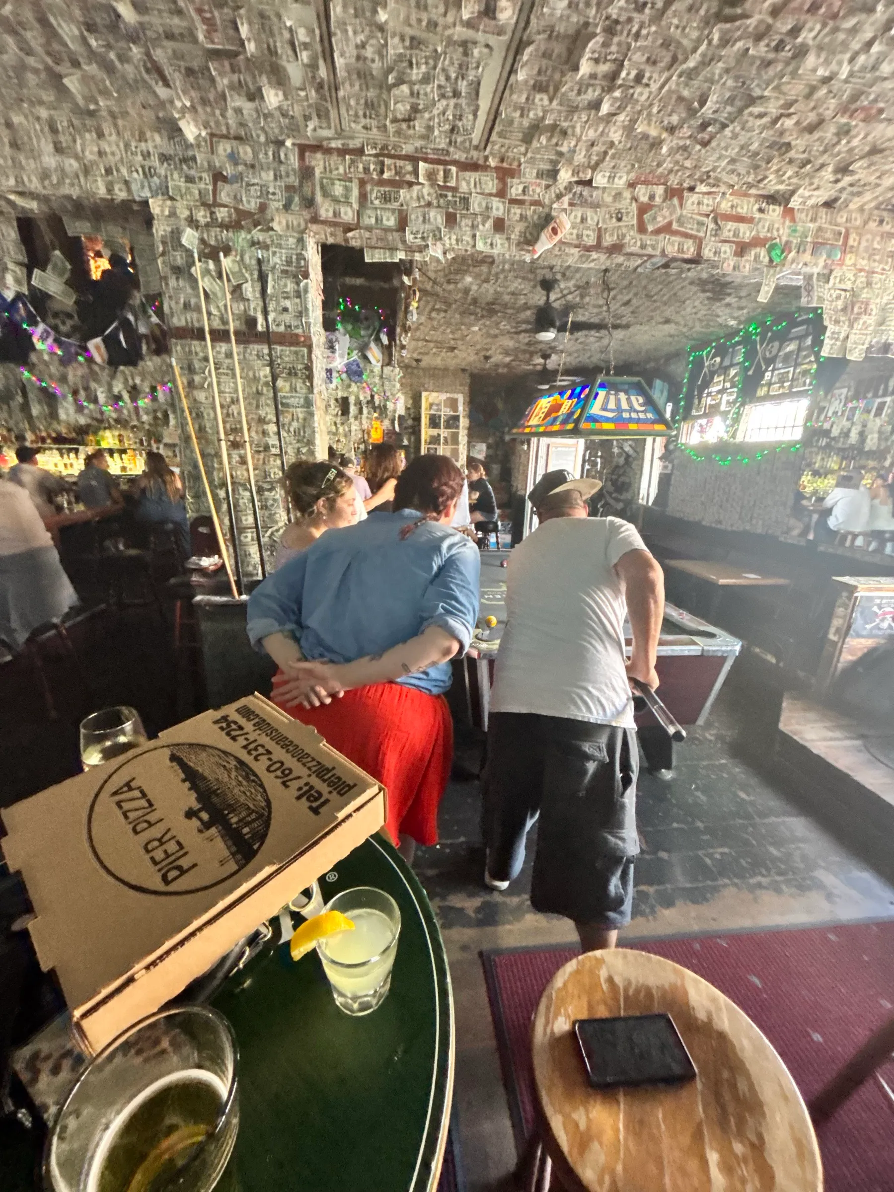 A dive bar with dollar bills covering the ceiling and a pool table